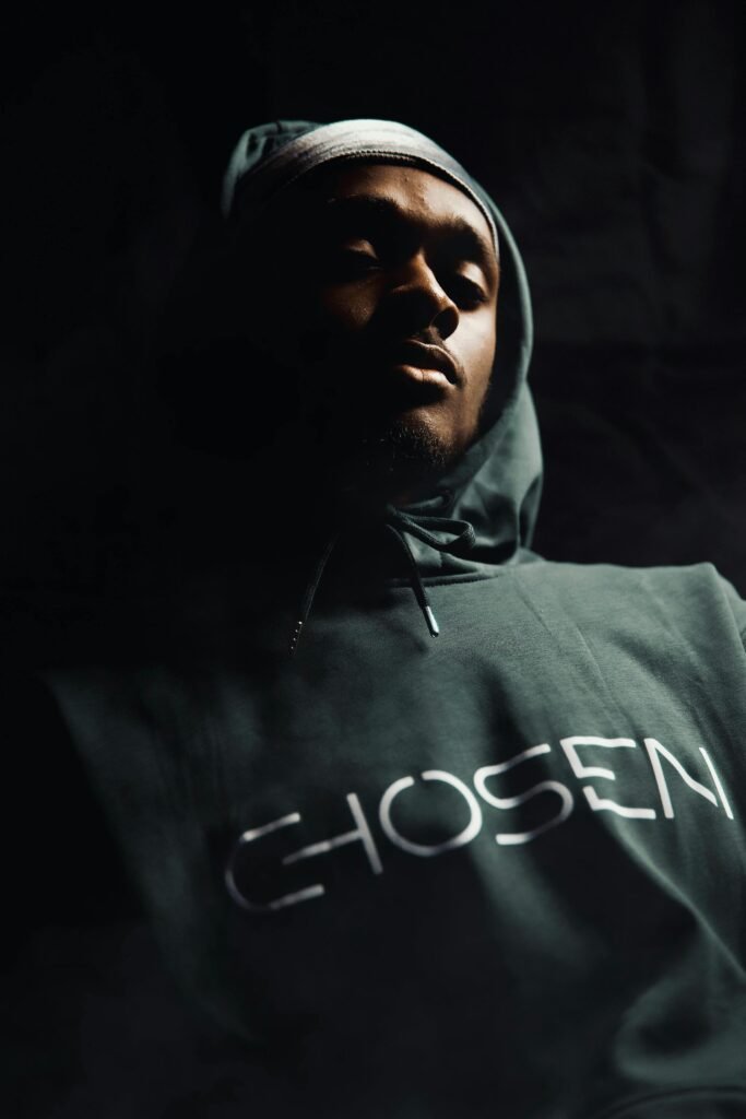 pexels photo 6925458 6925458 Dramatic portrait of a man in a hoodie with 'Chosen' text, captured indoors with a moody tone.